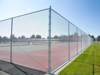 Galvanized chain link fabric and round posts tennis courts fencing beside grass land.